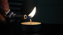 Eine Frau zündet mit einem Feuerzeug ein Teelicht an