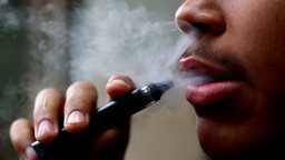 Ein Mann im Profil hält eine Vape, um die sich Dampfwolken gebildet haben