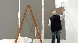 Ein älterer Mann streicht auf der Leipziger Messe eine Wand
