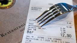 Ein Kassenbon mit einer Mehrwertsteuer von 19 Prozent für Speisen und Getränke liegt in einem Restaurant auf dem Tisch, darüber eine Gabel