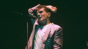 Der Musiker Falco mit Mikro, in einem rosafarbenen Sacko, während eines Auftritts im August 1986.