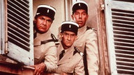 Szene aus "Louis' unheimliche Begegnung mit den Außerirdischen": Louis de Funès und seine Schauspielkollegen Michel Galabru und Maurice Risch schauen als Gendarm verkleidet grimmig aus dem Fenster