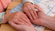 Eine Rentnerin hält die Hände ihres Sohnes