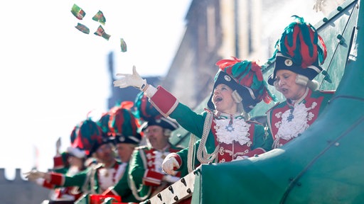 Karnevalisten auf einem Umzugswagen des Rosenmontagszugs 2025 auf der Kölner Severinstraße. Im Fokus des Bildes steht eine Frau, die gerade Kamelle in die Luft wirft.