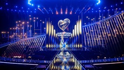 Der Blick auf die ESC-Bühne während eines ORF Medienupdates zum Eurovision Song Contest. Man sieht eine große, beleuchtete Bühne. Auf die Leinwand wird das Eurovision Song Contest Logo projiziert. 