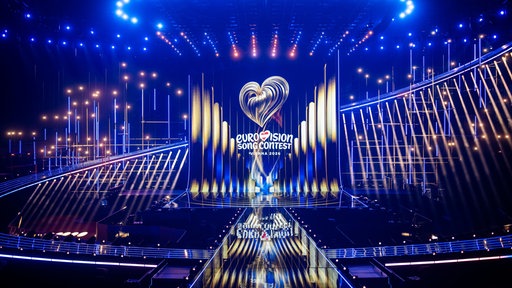 Der Blick auf die ESC-Bühne während eines ORF Medienupdates zum Eurovision Song Contest. Man sieht eine große, beleuchtete Bühne. Auf die Leinwand wird das Eurovision Song Contest Logo projiziert. 