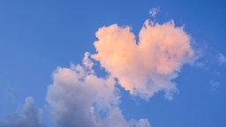 Eine rosafarbene, herzförmige Wolke am blauen Himmel