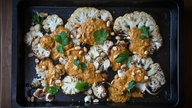 Von oben fotografiert: Eine Ofenform mit mehreren Scheiben Blumenkohl mit Kleksen Curry-Kokos-Sauce. Darüber gestreut sind Erdnüsse und Korianderblättchen. 