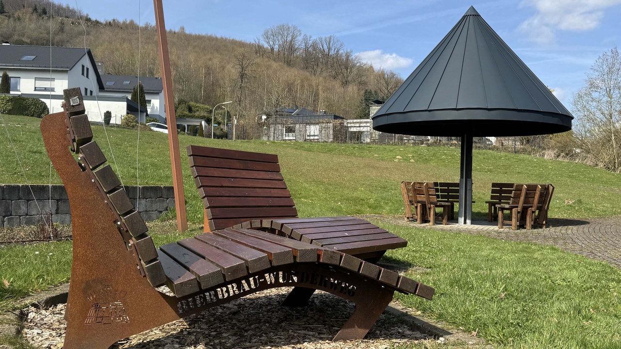 Zwei Liegen aus Holz auf einer Wiese. Daneben eine überdachte Sitzmöglichkeit