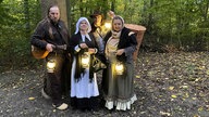 Verkleidete Darsteller mit Laternen im Wald