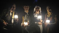 Vier verkleidete Darsteller mit Laternen in Dunkeln.