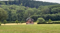 Ein einsames Häuschen steht auf einem Feld am Waldrand