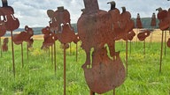 50 Metall-Silhouetten stehen aufgespießt auf Metallstäben auf einem Feld.