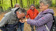 Ein Mann riecht an etwas Walderde, die ihm von einer Frau entgegengehalten wird. 