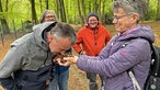 Ein Mann riecht an etwas Walderde, die ihm von einer Frau entgegengehalten wird. 