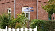 Straßenschilder, Boshamerweg und Kaiserwerthstraße, vor einem rotgeklinkertem Haus mit Sonnenblumen und weißem Zaun davor