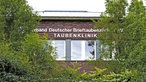 Zechenhäuser: Die Außenfassade eines höhergelegenen Gebäudes ragt oberhalb von Gebüsch umrahmt von Bäumen mit der Aufschrift "Verband Deutschter Brieftaubenzüchter e.V. Taubenklinki"