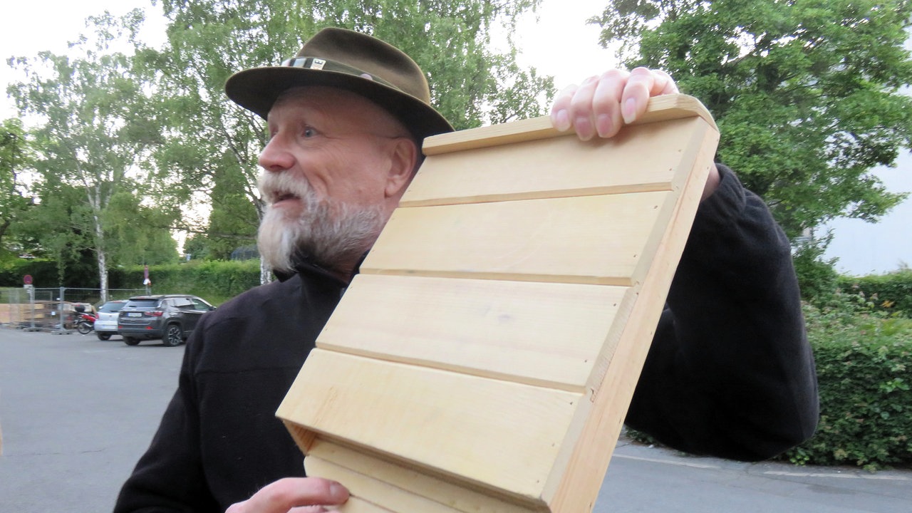 Manfred Kohlstadt hält einen selbst gebauten Fledermauskasten aus Holz in den Händen. 