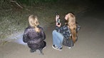 Zwei Mädchen hocken mit einem Ultraschalldetektor für Fledermäuse auf dem Boden.