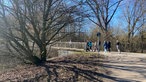Eine Gruppe Spaziergänger von etwas weiter weg von der Seite fotografiert. Sie gehen auf eine Brücke zu. 