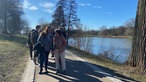 Die Teilnehmer von "Ideen im Gehen" auf einem Fußweg. Alle sind sichtlich in Gesprächen mit ihren Mitspazierenden. Rechts im Bild ist der Aasee zu sehen.