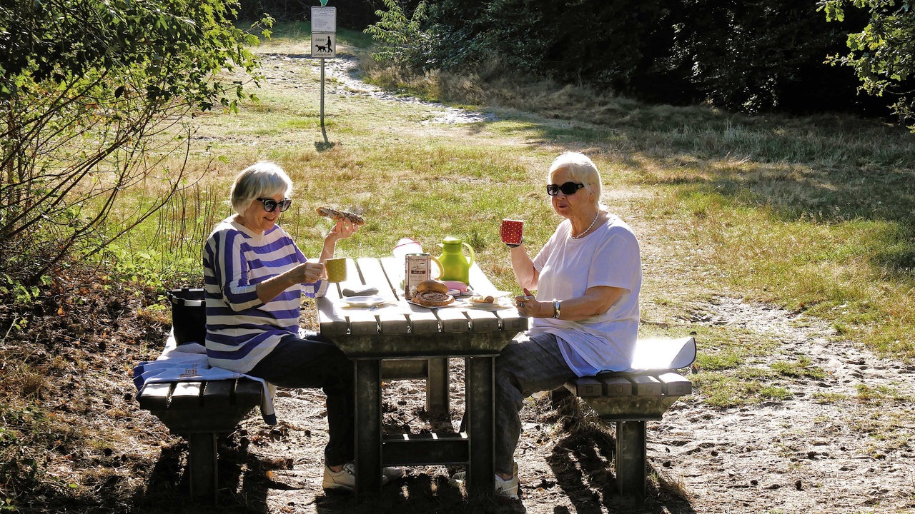 Westruper Heide: Zwei Frauen frühstücken auf dem Waldweg an einem Rastplatz in der Sonne