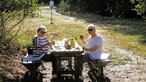 Westruper Heide: Zwei Frauen frühstücken auf dem Waldweg an einem Rastplatz in der Sonne
