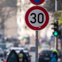 Auto- und Radfahrer passieren ein Verkehrschild in einer Zone mit 30 Kilometern Geschwindigkeitsbeschränkung