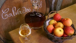 EIn Glas und eine Flasche Calvados auf einem Tisch mit Äpfeln