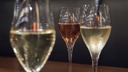 Weisser und rosefarbener Cremant in Gläsern auf einem Holztisch.