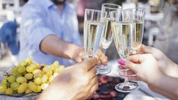 Vier Menschen stoßen an einem Tisch mit Champagnergläsern an