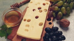 Emmentaler mit Löchern, auf einem Teller angerichtet, dazu Trauben und Honig.