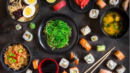 Ein dunkler Tisch, gedeckt mit japanischen Spezialitäten, wie Sushi, Ramen und Miso Suppe.