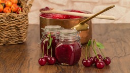 Kirschmarmelade im Glas, im Hintergrund ein Kupfertopf. 