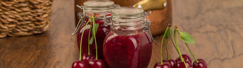 Kirschmarmelade im Glas, im Hintergrund ein Kupfertopf. 