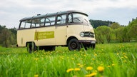 Ein alter Van mit der Aufschrift "Landfrauenküche" auf einer grünen Wiese.