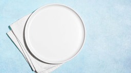 Leerer weißer Teller auf hellblauem Untergrund. 