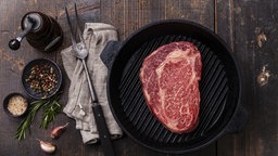 Ein frisches Stück Black Angus Rindfleisch in einer Bratpfanne auf einem Holztisch.