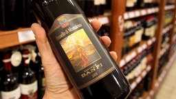 EIne Hand hält vor einem Weinregal eine Flasche mit dem Etikett nach vorne 