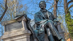 Brandenburg, Neuruppin: Als rastender Wanderer mit Stock und Hut wird der Dichter Theodor Fontane als Bronze-Denkmal im Stadtzentrum dargestellt.