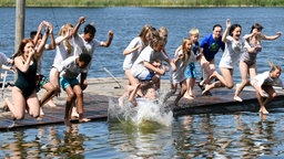 Eine Gruppe von Kindern und Jugendlichen springt bei einer Jugendfreizeit von einem Steg in einen Badesee