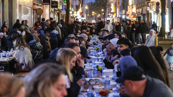 Zahlreiche Menschen sitzen zum Fastenbrechen in der Kölner Keupstraße an einem langen Tisch und essen gemeinsam.