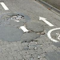 Das Beitragsbild zeigt eine Straße mit vielen Straßenschäden. 