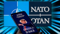 Website des Weißen Hauses ist auf einem Mobiltelefon angezeigt, im Hintergrund ist NATO-OTAN zu sehen. 