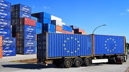 Container mit EU-Fahne auf einem LKW, im Hintergrund gestapelte Container.