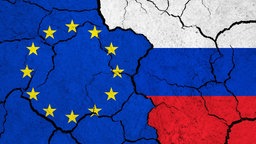Flaggen der Europäischen Union und Russlands auf rissiger Oberfläche.