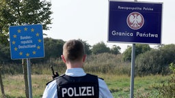 Bundespolizist steht vor den Grenzschildern für Deutschland und Polen.