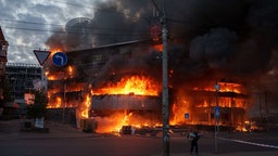 Mann trägt Kiste aus einem brennenden Handelszentrum nach einem russischen Angriff auf Kiew, 24.05.2026.