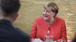 Zehn Jahre nach der Fluchtbewegung trifft Angela Merkel erstmals öffentlich auf Geflüchtete, deren Leben durch ihre Entscheidung geprägt wurde.