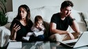 Mother using smart phone while father working on laptop with son sitting at home